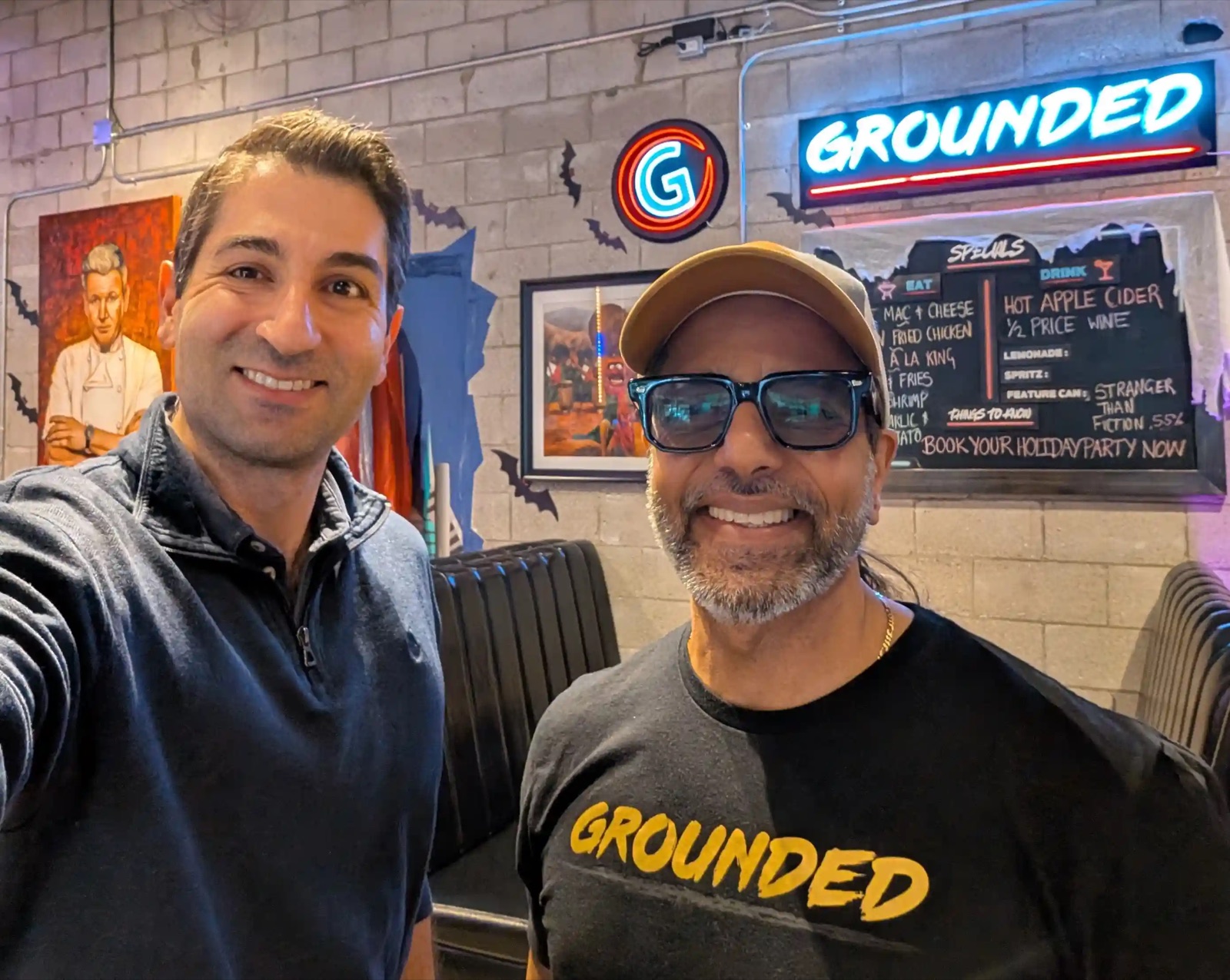 Elias Hage with Amir of Grounded Kitchen inside the restaurant, with the Grounded neon sign and specials board behind them.