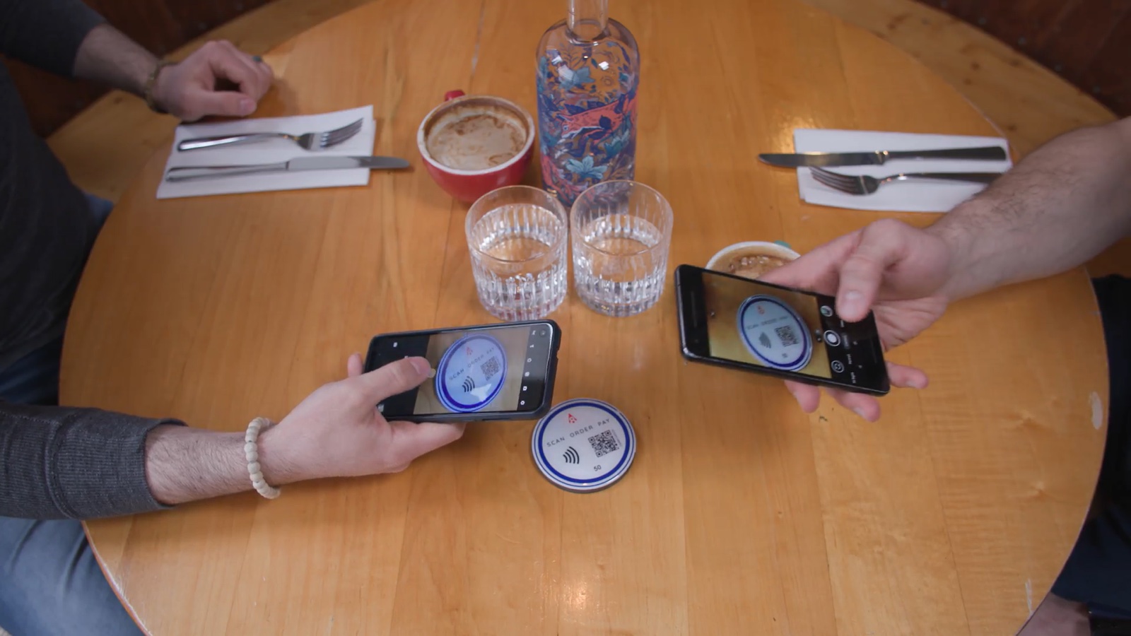 Two phones scanning a QR code on a round table coaster that reads Scan, order, pay